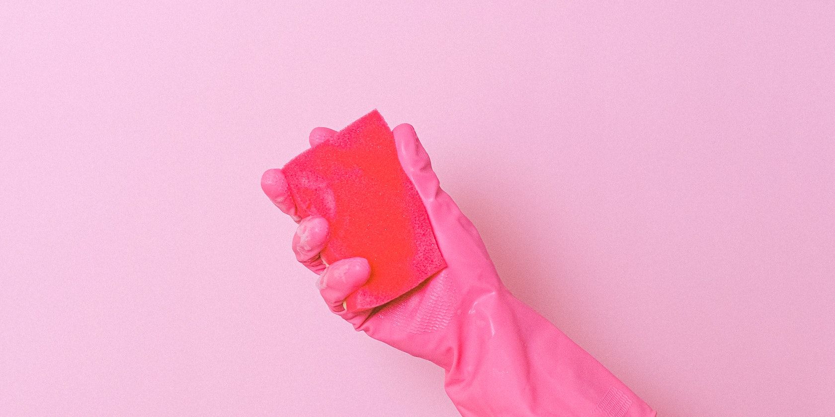 Mani guantate rosa che tengono una spugna rossa