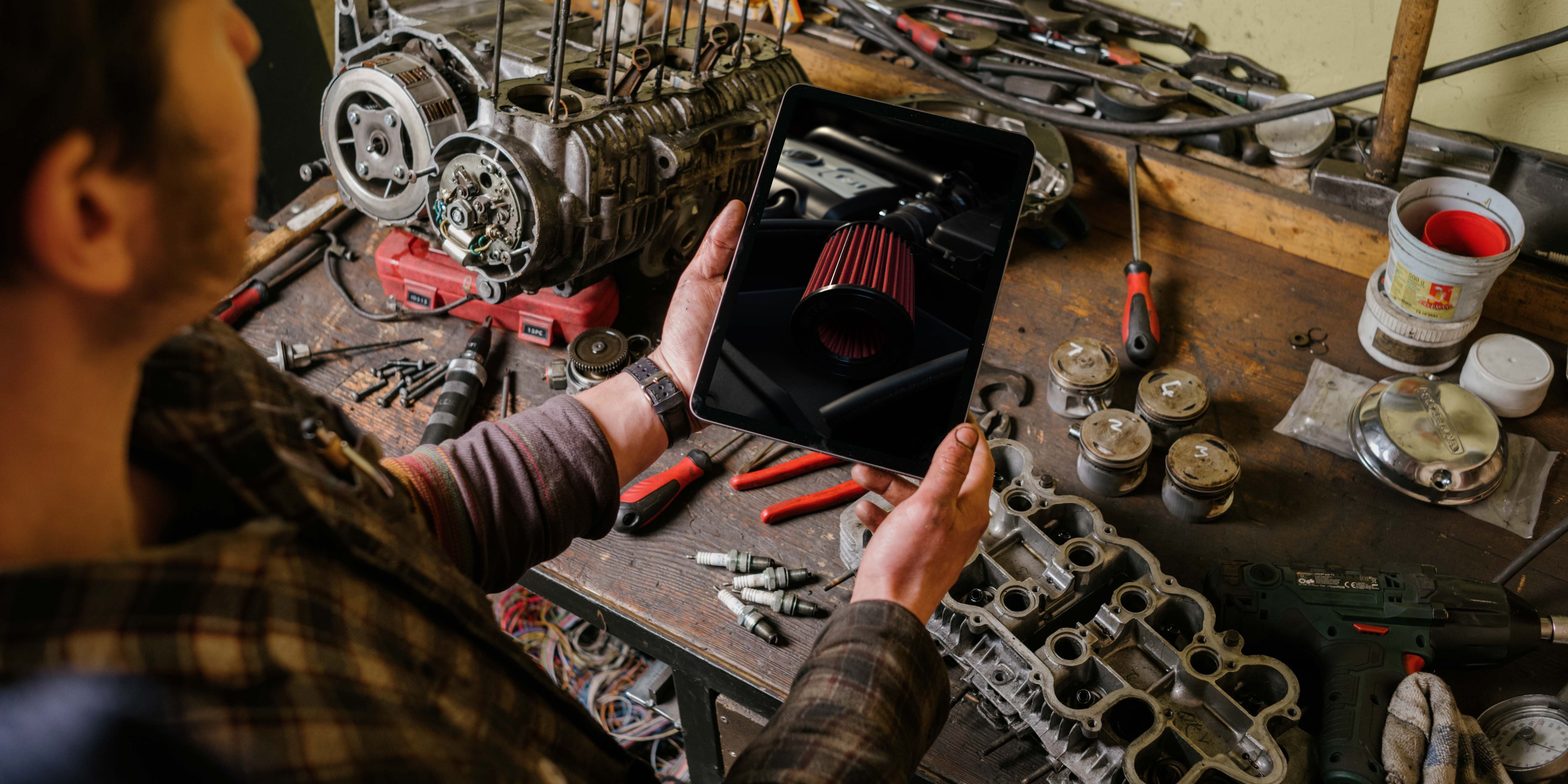 Meccanico che lavora in garage, utilizzando un iPad per riparare il motore di un'auto